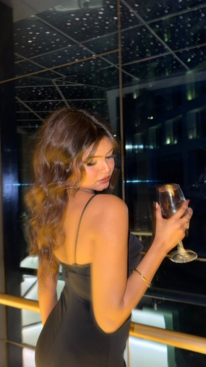 Vaishnavi Kadekar in a black dress holding a wine glass on a rooftop at night