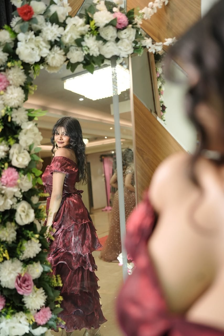 Vaishnavi Kadekar in a maroon tiered gown, mirror reflection among flowers